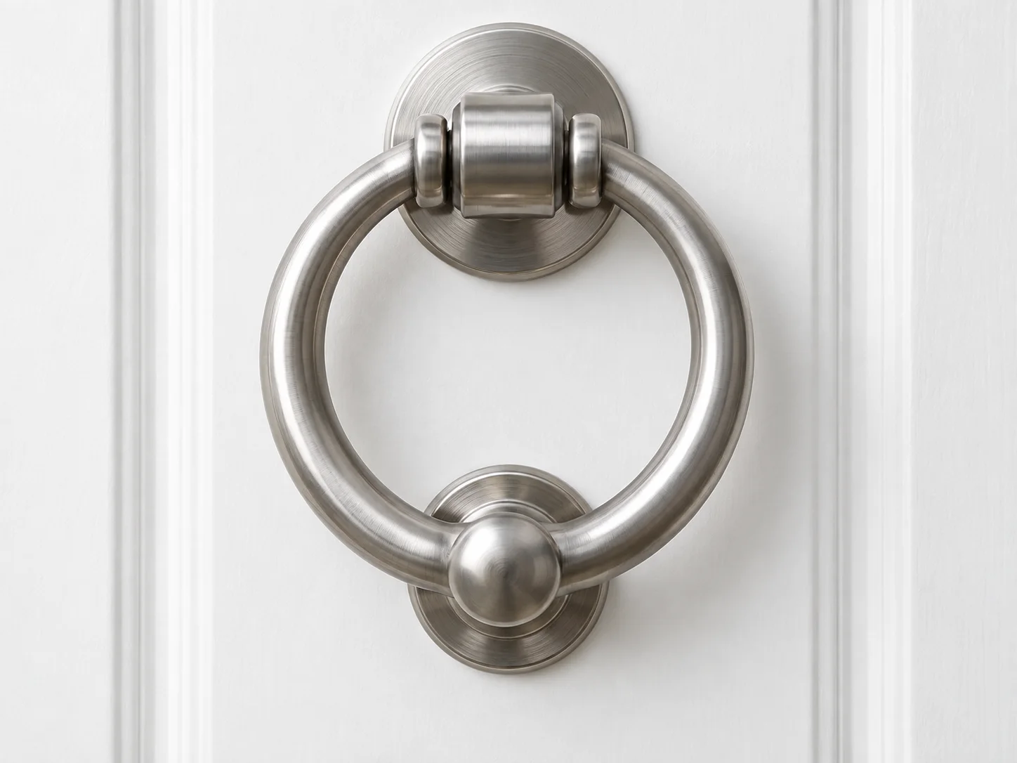 Brushed-metal ring door knocker with a pivot and strike plate on a white door.