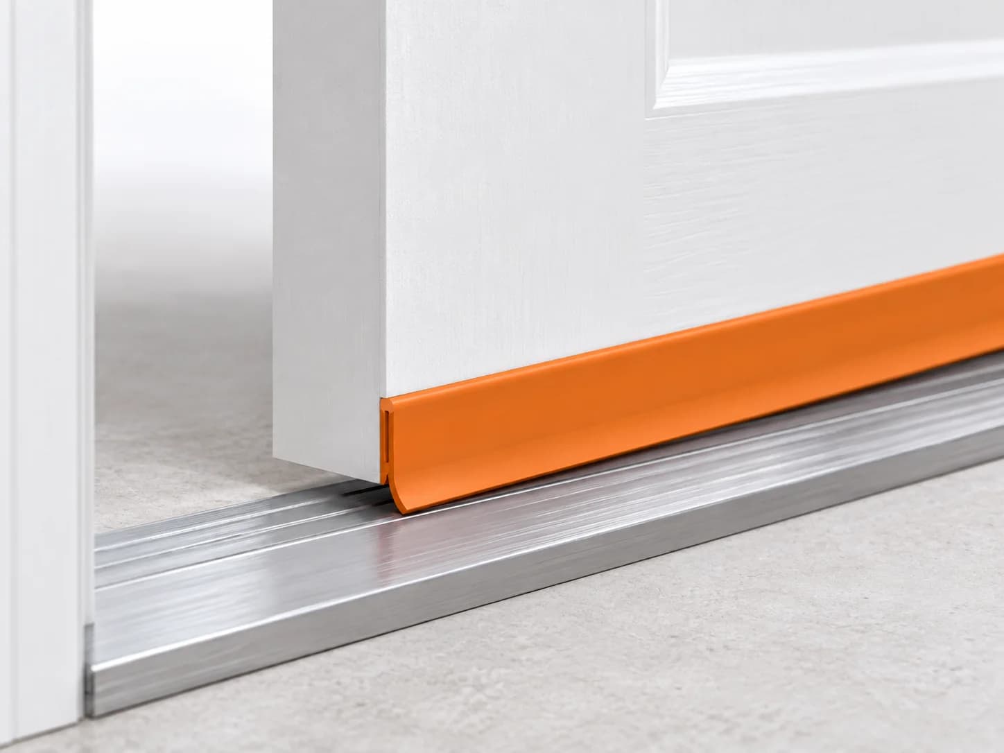 Bottom of a door with the flexible sweep attached to the slab highlighted orange above the threshold.