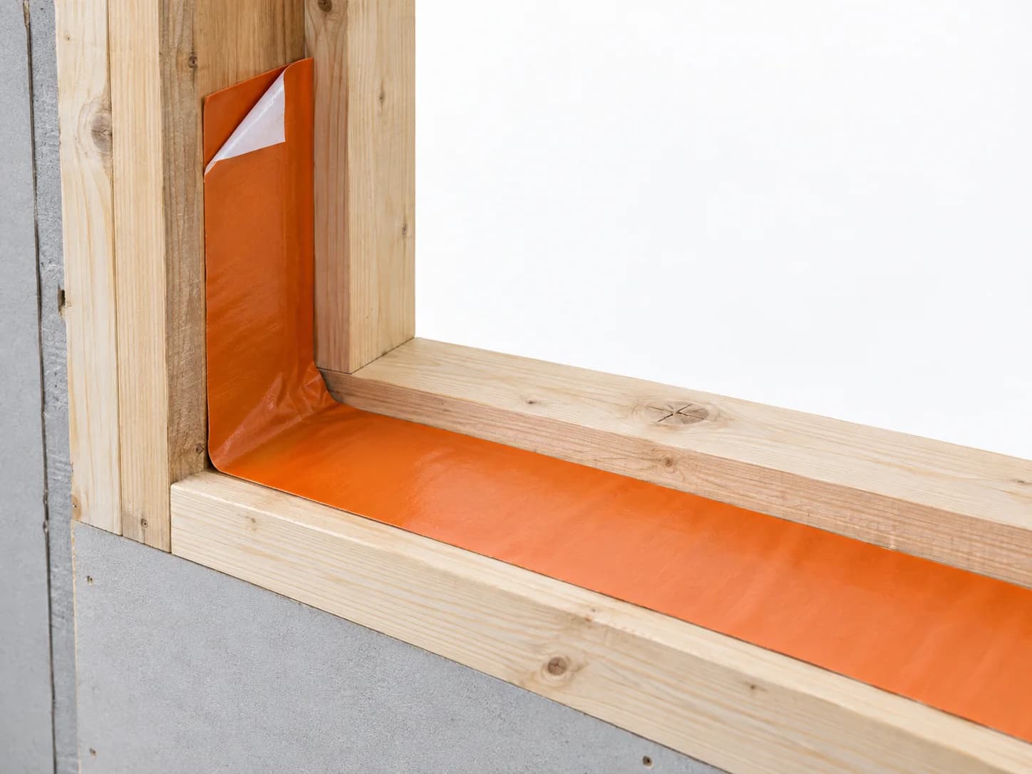 Lower timber window opening wrapped with flashing tape highlighted orange at the sill and jamb corner.