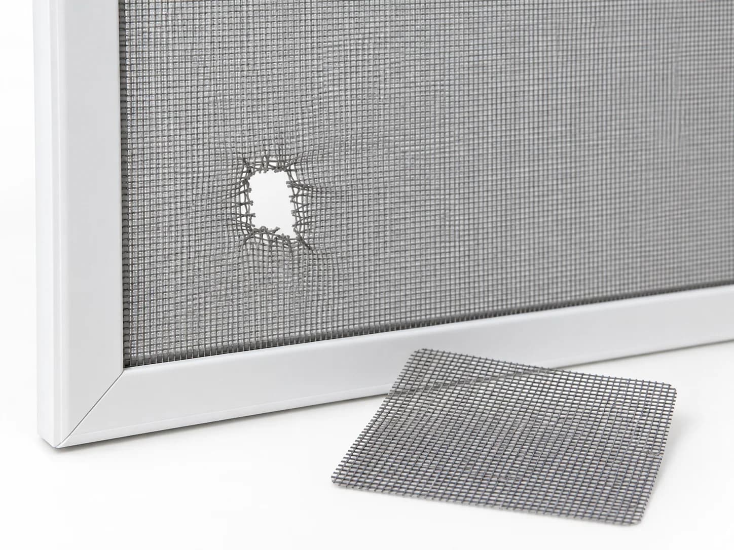 Insect screen with a small tear and a matching mesh repair patch beside it.