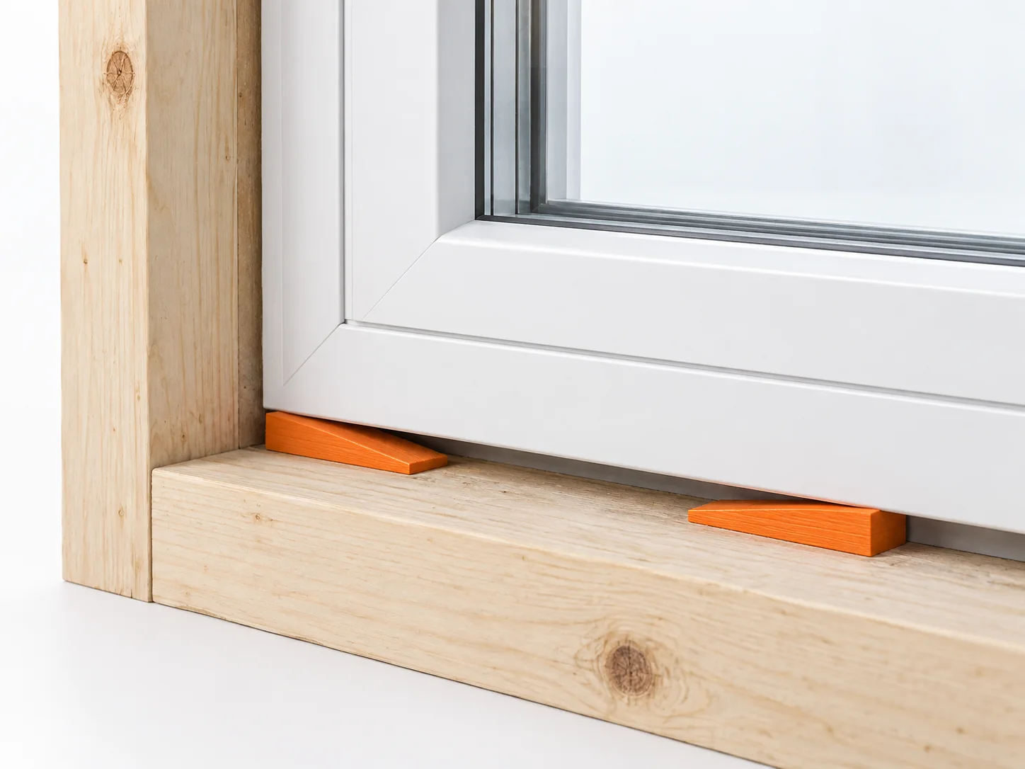 Window corner supported in a timber opening by opposing tapered shims highlighted orange.